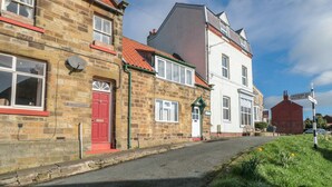 Une rue bordée de bâtiments traditionnels en pierre, un ciel dégagé et un panneau indiquant les directions vers Hawsker et Whitby.