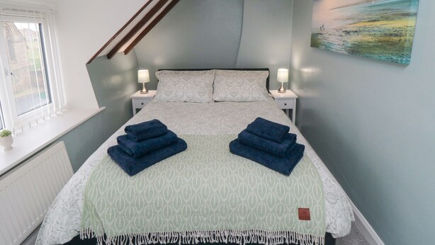 Une chambre à coucher avec un lit, deux tables de chevet, une fenêtre et un tableau au mur.