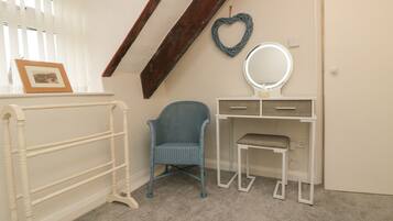 A room with a white vanity, a blue chair, a white bench, a wooden beam, a heart-shaped decoration, and a framed picture on the wall.
