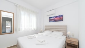 Una cama bien hecha con sábanas y toallas blancas, una mesita de noche con una lámpara, y un cuadro de un atardecer en la pared.