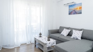 Una sala de estar moderna con un sofá gris, dos almohadones estampados, una mesa de centro de madera con mantel blanco y un cuadro de un atardecer en la pared.