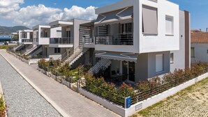 Un moderno edificio residencial de varios pisos con balcones, camino pavimentado y jardín ajardinado.