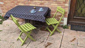 Una mesa dispuesta con dos tazas y platillos azules, una cuchara dorada y un adorno sobre un mantel estampado. Dos sillas verdes están colocadas alrededor de la mesa.