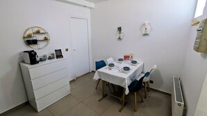 Un comedor con una mesa dispuesta para cuatro personas, una máquina de café y un armario blanco con cajones.