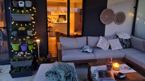 A cozy living area with a sofa, a coffee table, and a bookshelf with plants and lights. - JO bel Appart Proche Versailles (Louveciennes)