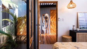 A modern bedroom with a wooden floor, a bed, a hanging light fixture, and a view of the outside. - Boho Oasis in the heart of town (Tamarindo)