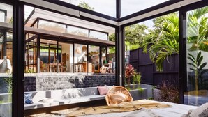A modern bedroom with a large glass wall, a bed, and a seating area with a view of the backyard. - Boho Oasis in the heart of town (Tamarindo)