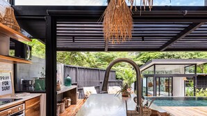 A modern kitchen with a large island, a dining area with a view of a swimming pool, and a sign that reads "PRAY FOR SURF". - Boho Oasis in the heart of town (Tamarindo)