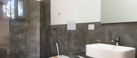 Un baño moderno con un lavamanos grande de color blanco, un inodoro y una zona de ducha.