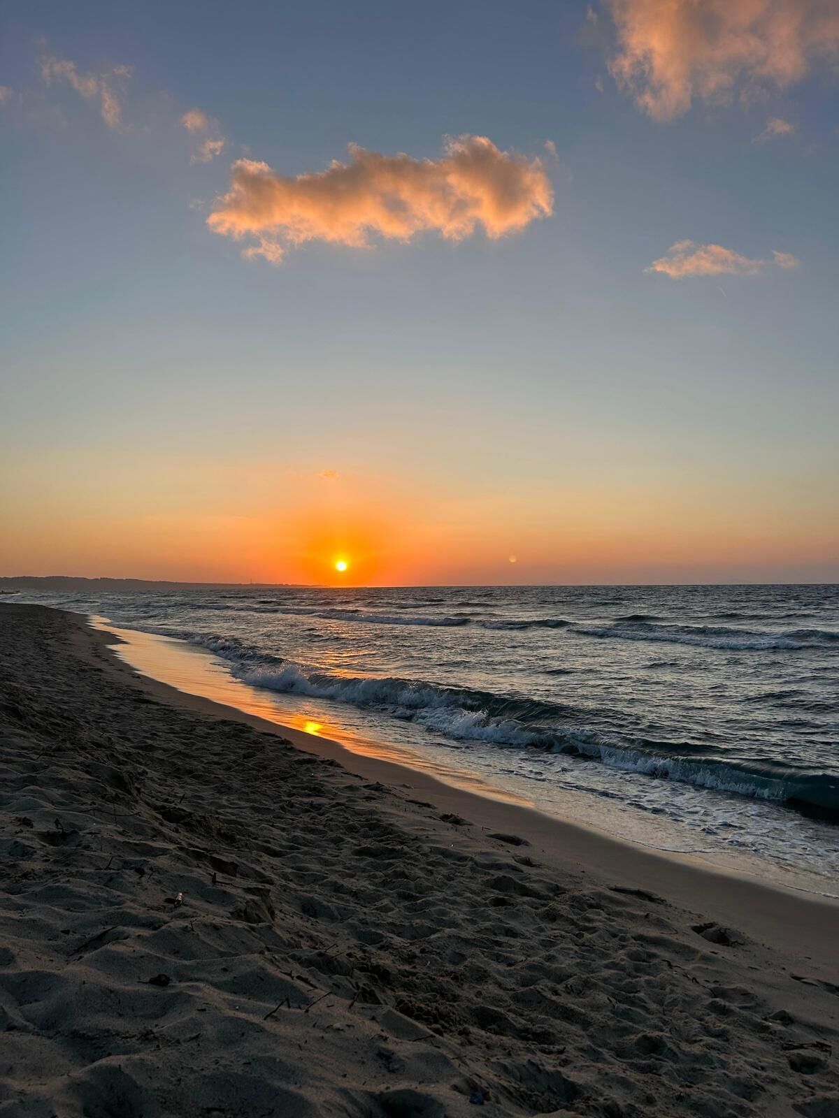 A beach with a sunset over the ocean, sandy shore, and waves.