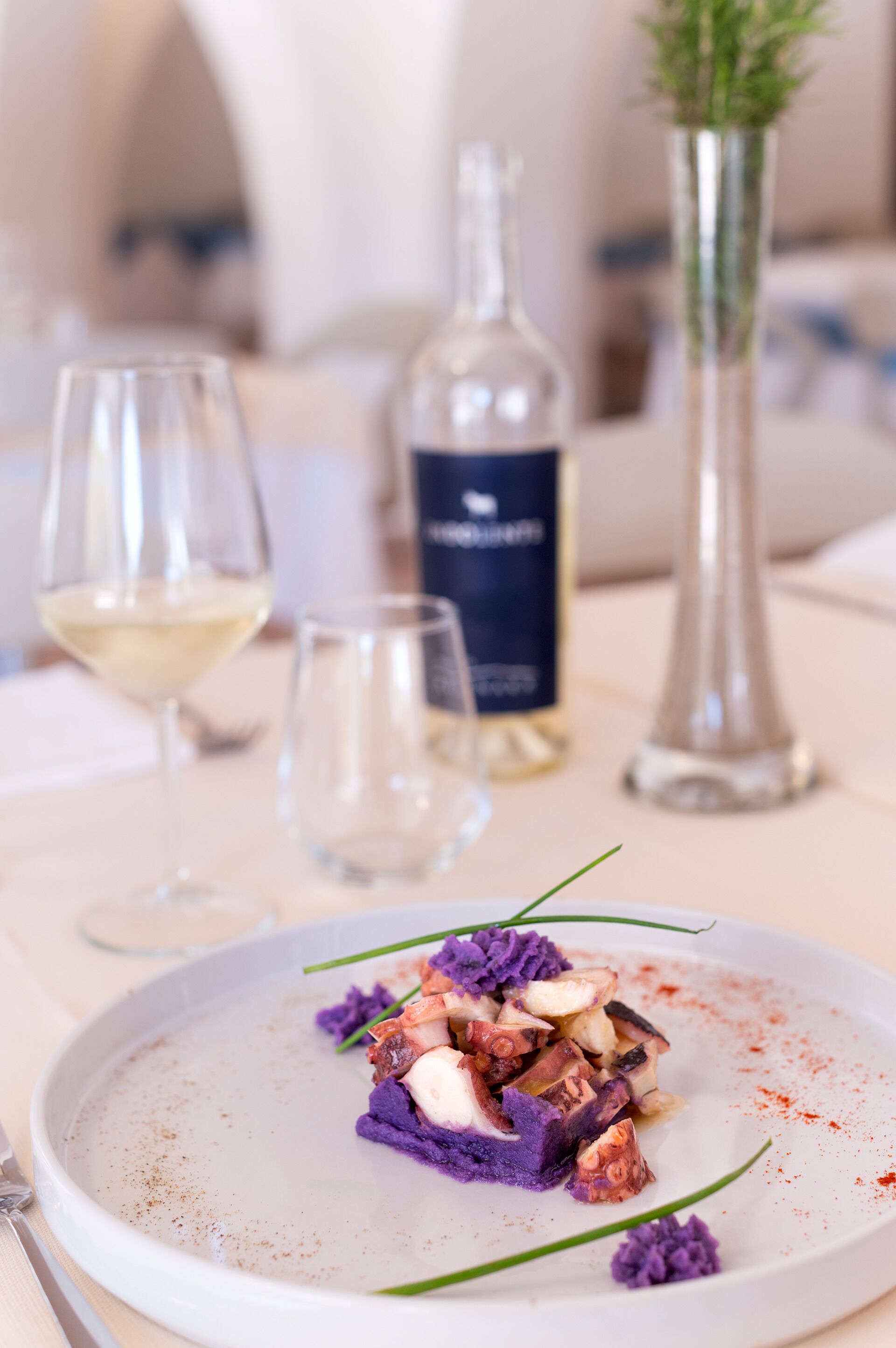 A dining table with a plate of food, a bottle, and two glasses.