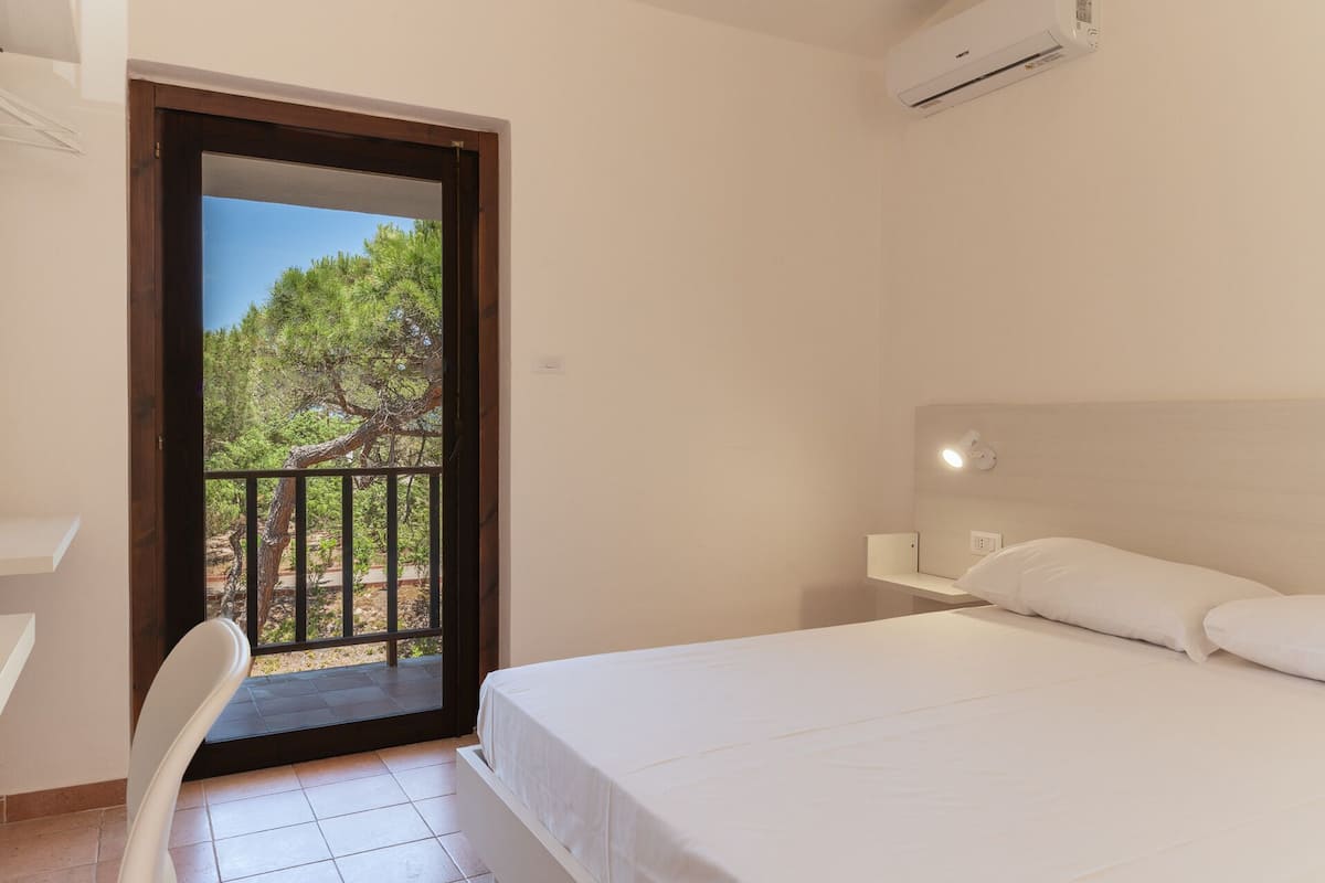 Une chambre avec un lit, une chaise, un balcon doté d’une rambarde et un appareil de climatisation.