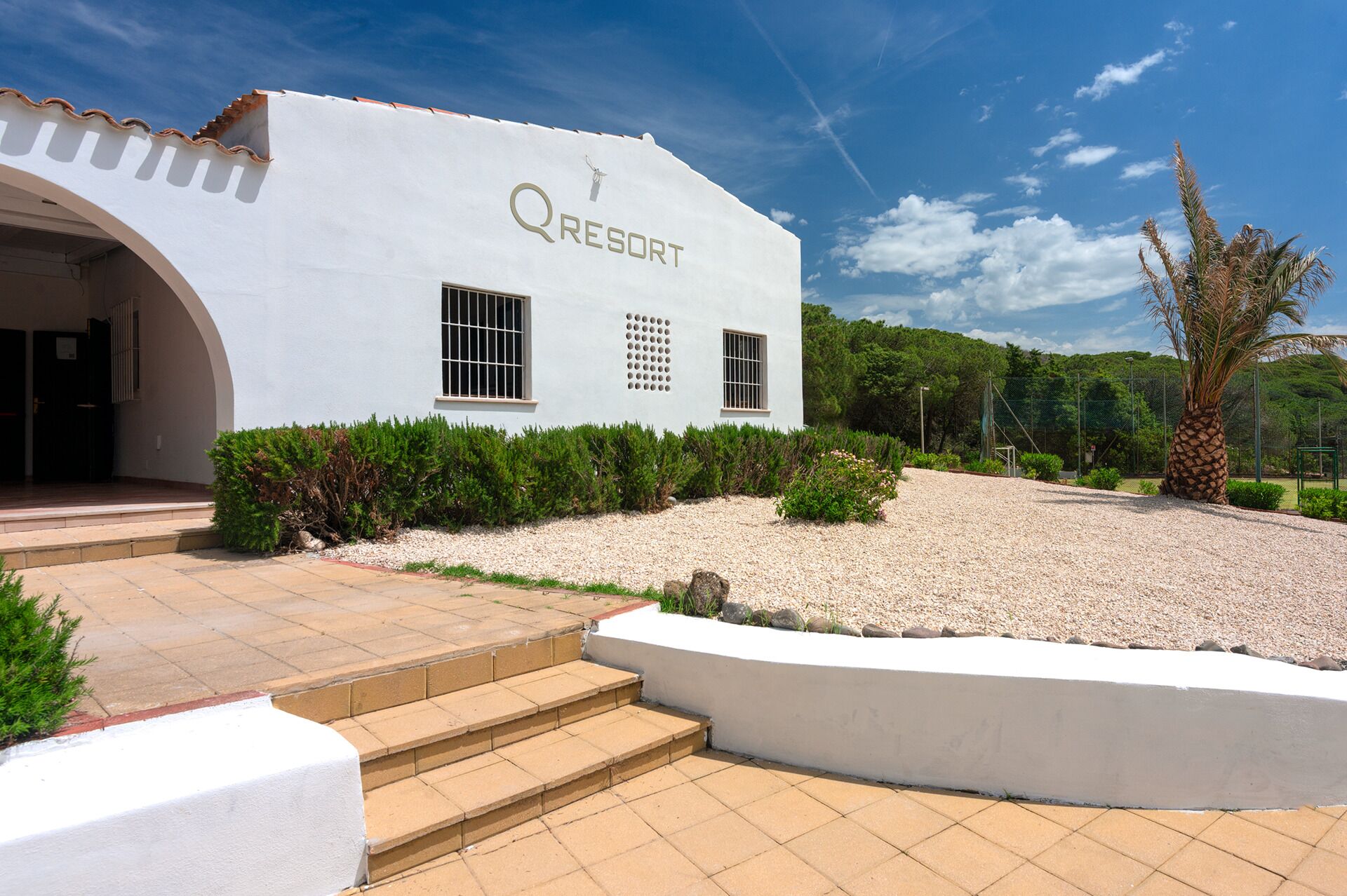 A white building with the sign 'QRESORT' and a landscaped entrance area with steps leading up to the door.