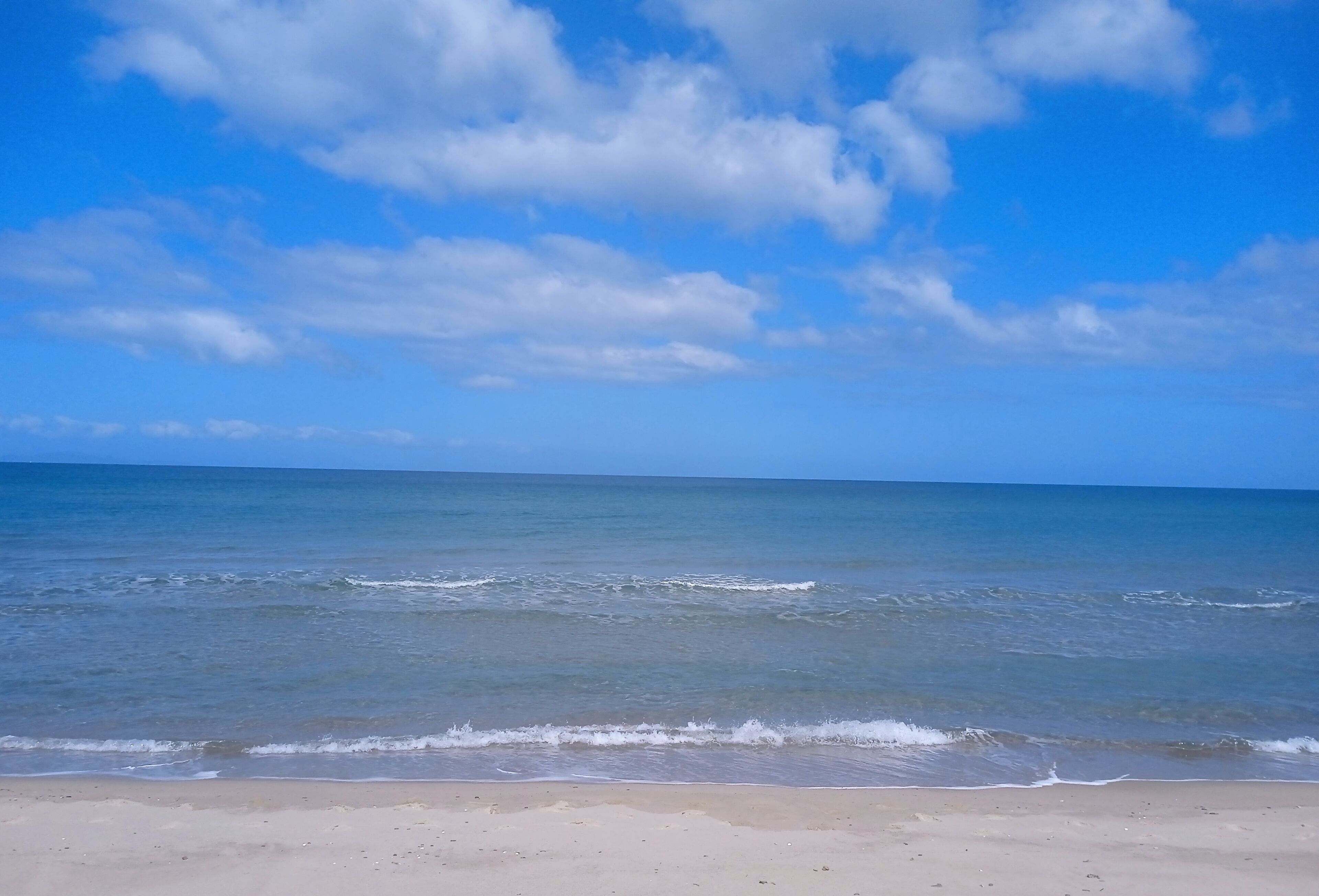 Ein Strand mit blauem Himmel und ruhiger Brandung.