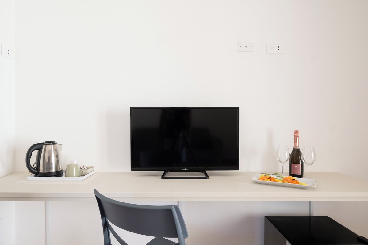 Habitación moderna con televisión de pantalla plana, tetera, plato con comida y botella de vino.