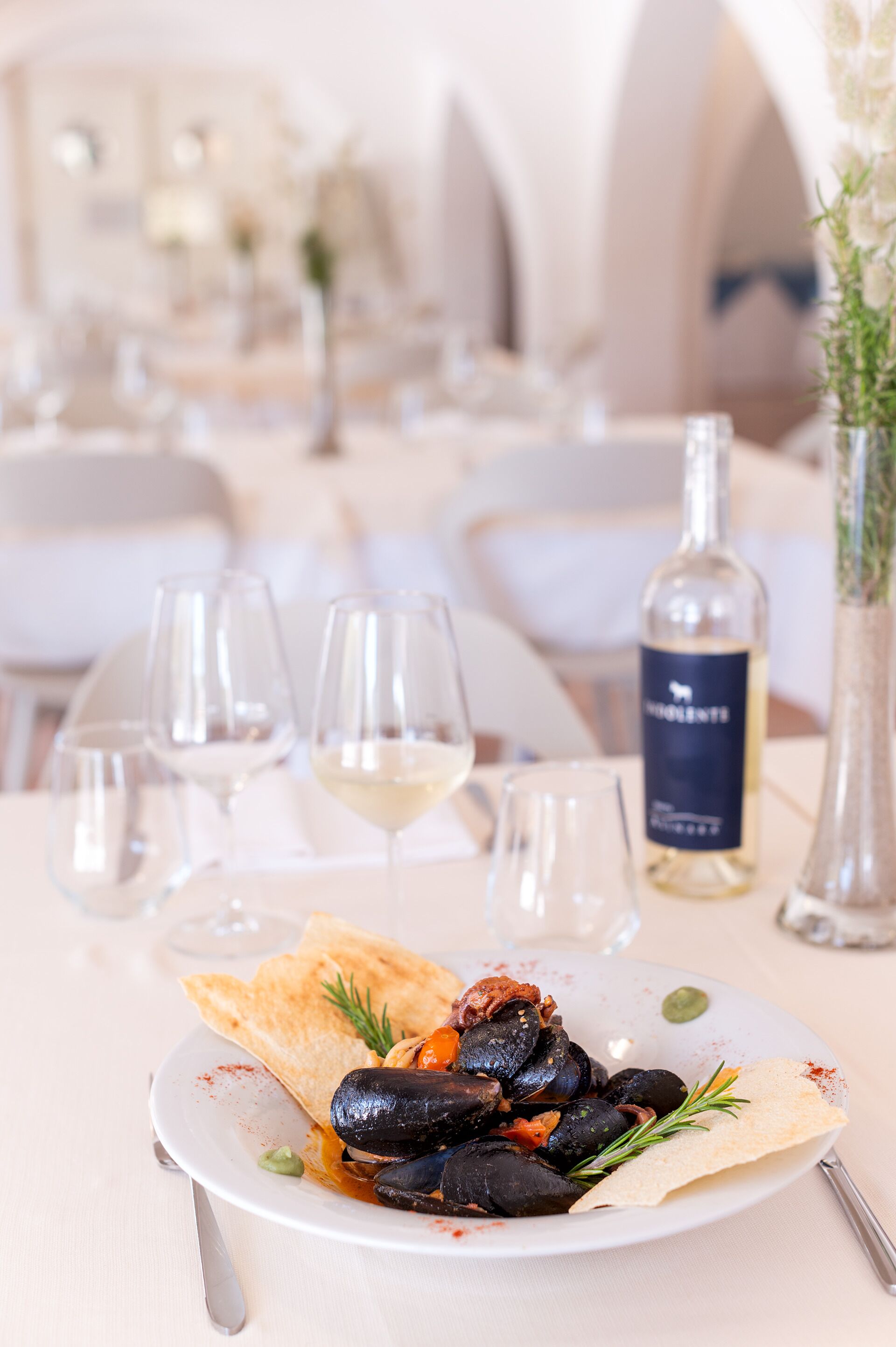 Une table à manger avec une assiette de moules, des verres à vin et une bouteille de vin.