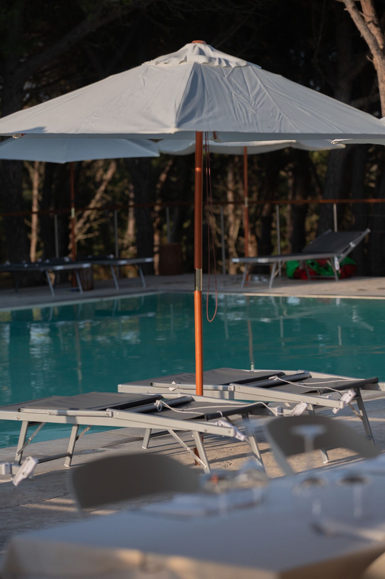 A poolside area with a white umbrella, lounge chairs, and a pool.