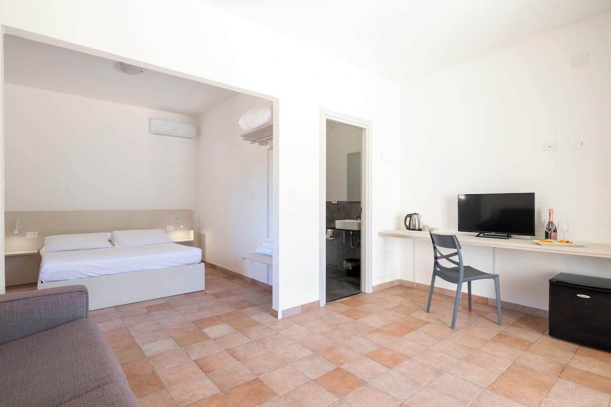 Une chambre comprenant un lit, un bureau, une chaise, une télévision et une petite kitchenette.