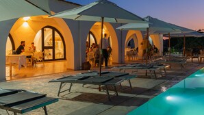 A poolside area with sun loungers and umbrellas, a restaurant with outdoor seating, and a pool with a blue cover. - Q Resort (Sorso)