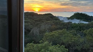 Blick aus dem Fenster auf einen Sonnenuntergang über einer bewaldeten Landschaft.