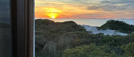 A window view of a sunset over a forested landscape.