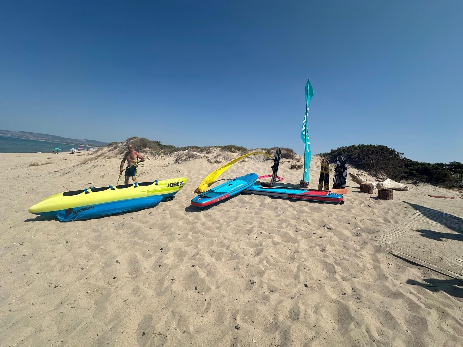 A sandy beach with several kayaks and a flagpole.