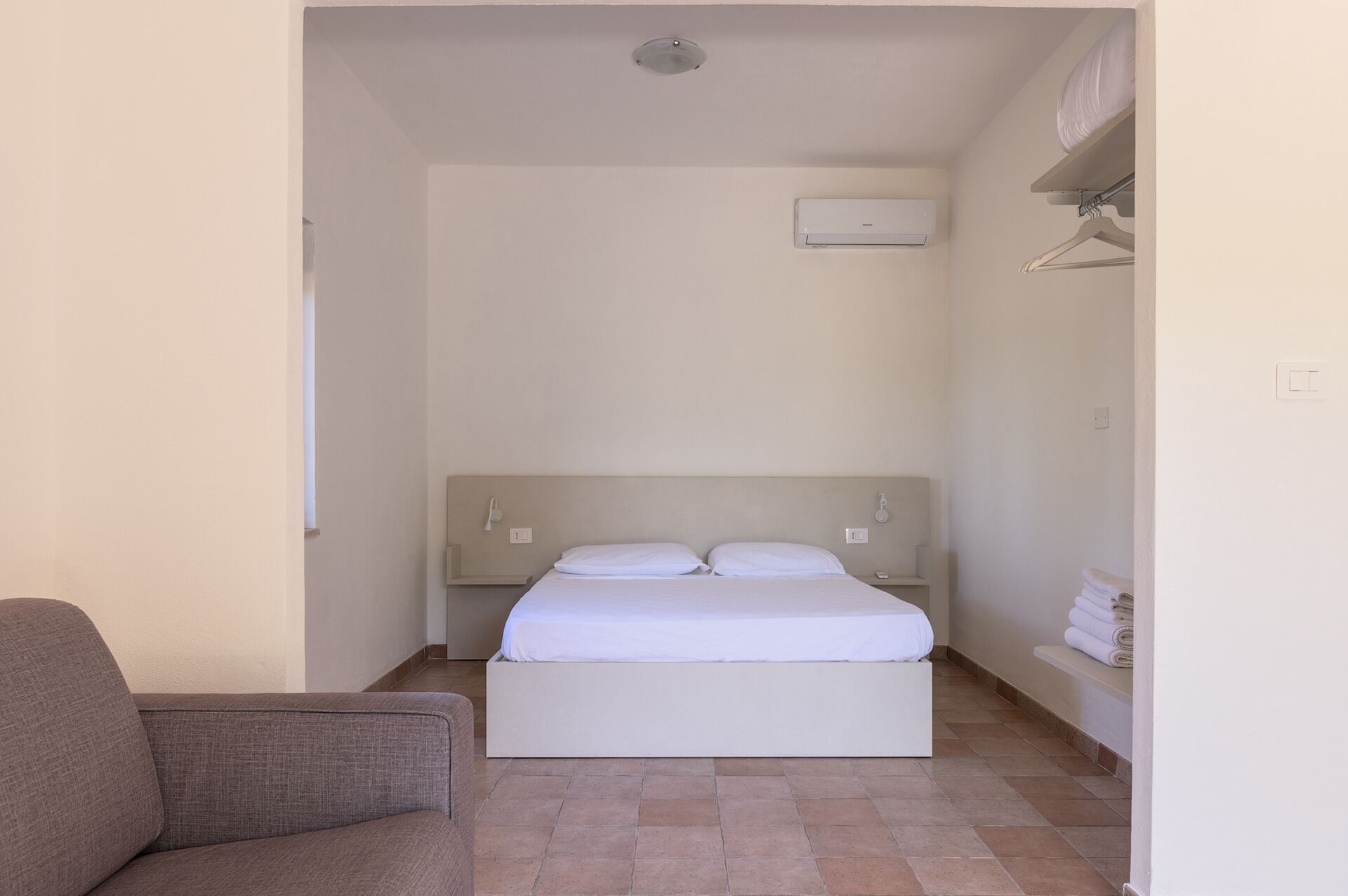 Una camera da letto con un letto, un comodino, un appendiabiti a parete e un climatizzatore.