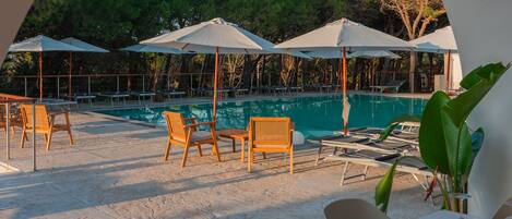 A poolside area with lounge chairs and umbrellas, a pool, and a dining table set for two.