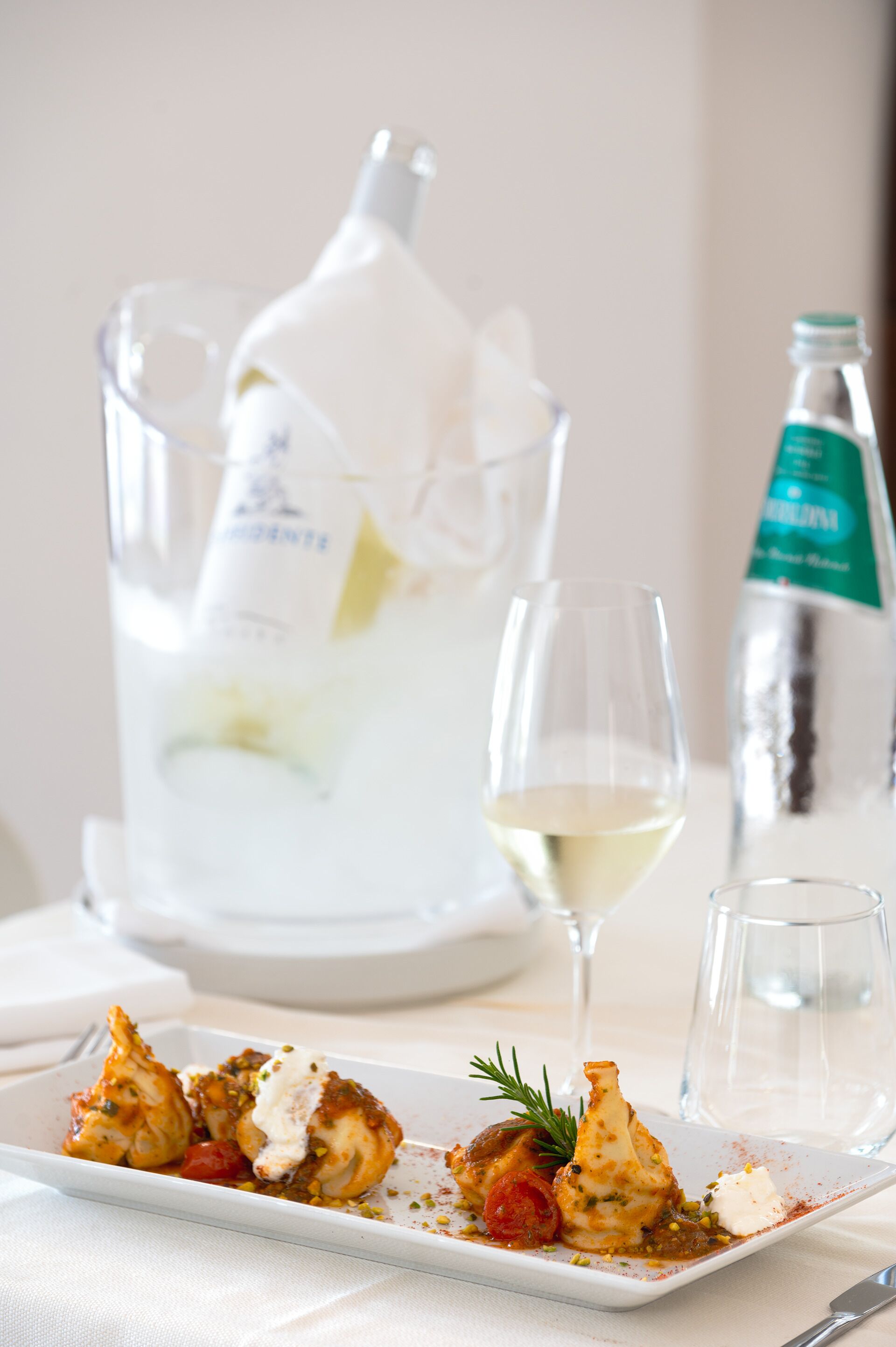 Une assiette blanche contenant de la nourriture, un verre à vin et une bouteille d’eau sont posés sur une table.