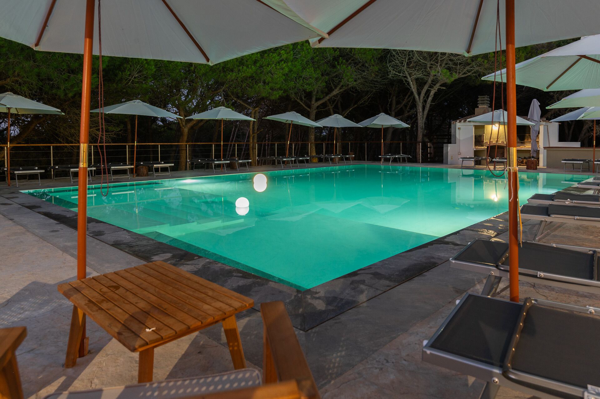 A swimming pool with lounge chairs and umbrellas, surrounded by trees.