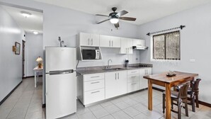 A compact kitchen with white cabinets, a microwave, a refrigerator, a ceiling fan, and a dining table with chairs. - Charming  1bedroom 5 mins to beach (Tamarindo)