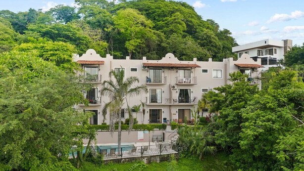 A multi-story hotel with balconies, surrounded by lush greenery and a pool. - Charming  1bedroom 5 mins to beach (Tamarindo)