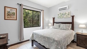 A bedroom with a large bed, an air conditioning unit, a window with curtains, and a ceiling fan. - Charming  1bedroom 5 mins to beach (Tamarindo)