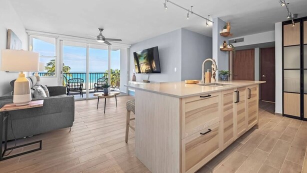 A modern kitchen with a large island, wooden cabinets, and a view of the ocean. - Azure Breezes | Modern Sanctuary by the Beach (Carolina)