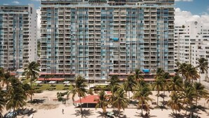 A high-rise hotel with multiple balconies, a beach in the foreground, and palm trees. - Azure Breezes | Modern Sanctuary by the Beach (Carolina)