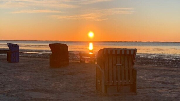A beach scene with a sunset, featuring three beach chairs and a small table. - Ferienhaus Muschel mit Garten an der Nordsee (Dornum)