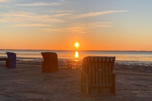 Eine Strandansicht mit Sonnenuntergang, mit drei Liegestühlen und einem kleinen Tisch.