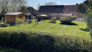 A residential area with a small wooden shed, a bicycle, and a yellow umbrella in the yard. - Ferienhaus Muschel mit Garten an der Nordsee (Dornum)