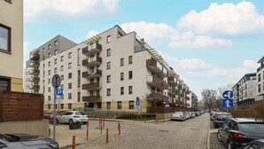 A multi-story residential building with balconies, a parking area, and directional signs.