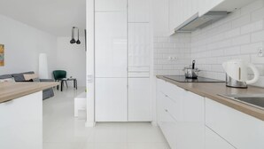 A modern kitchen with white cabinets, a wooden countertop, and a kettle.
