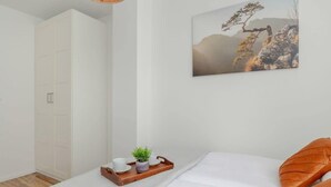 A bedroom with a bed, a wooden tray with cups and a plant, and a painting on the wall.