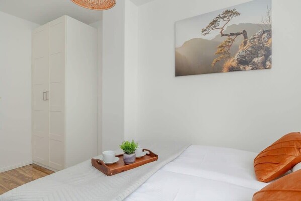 Un dormitorio con una cama, una bandeja de madera con tazas y una planta, y un cuadro en la pared.