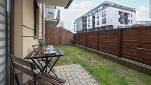 A balcony with a table and chairs, a wooden fence, and a building in the background.