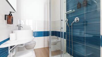 Un baño moderno con cabina de ducha de vidrio, un lavamanos blanco y pared con azulejos azules.