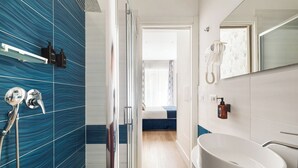 A modern bathroom with a large bathtub, a shower with a handheld showerhead, and a mirror with a telephone.
