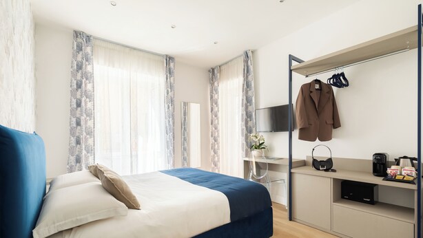 A modern bedroom with a bed, a desk, a TV, and a coat rack.