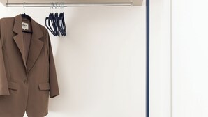 A neatly organized closet with a hanging coat, a pair of headphones, a coffee maker, and a small box of Kleenex.