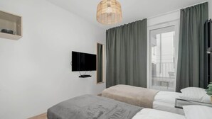 Una habitación de hotel moderna con dos camas, un televisor, una lámpara de mimbre y un ventanal con cortinas.
