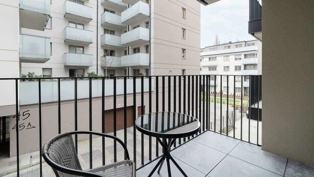 Un balcón con una mesa de vidrio y dos sillas, con vista a un edificio residencial.