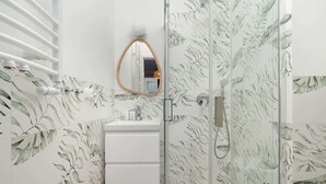 Un baño con lavamanos blanco, espejo y zona de ducha.